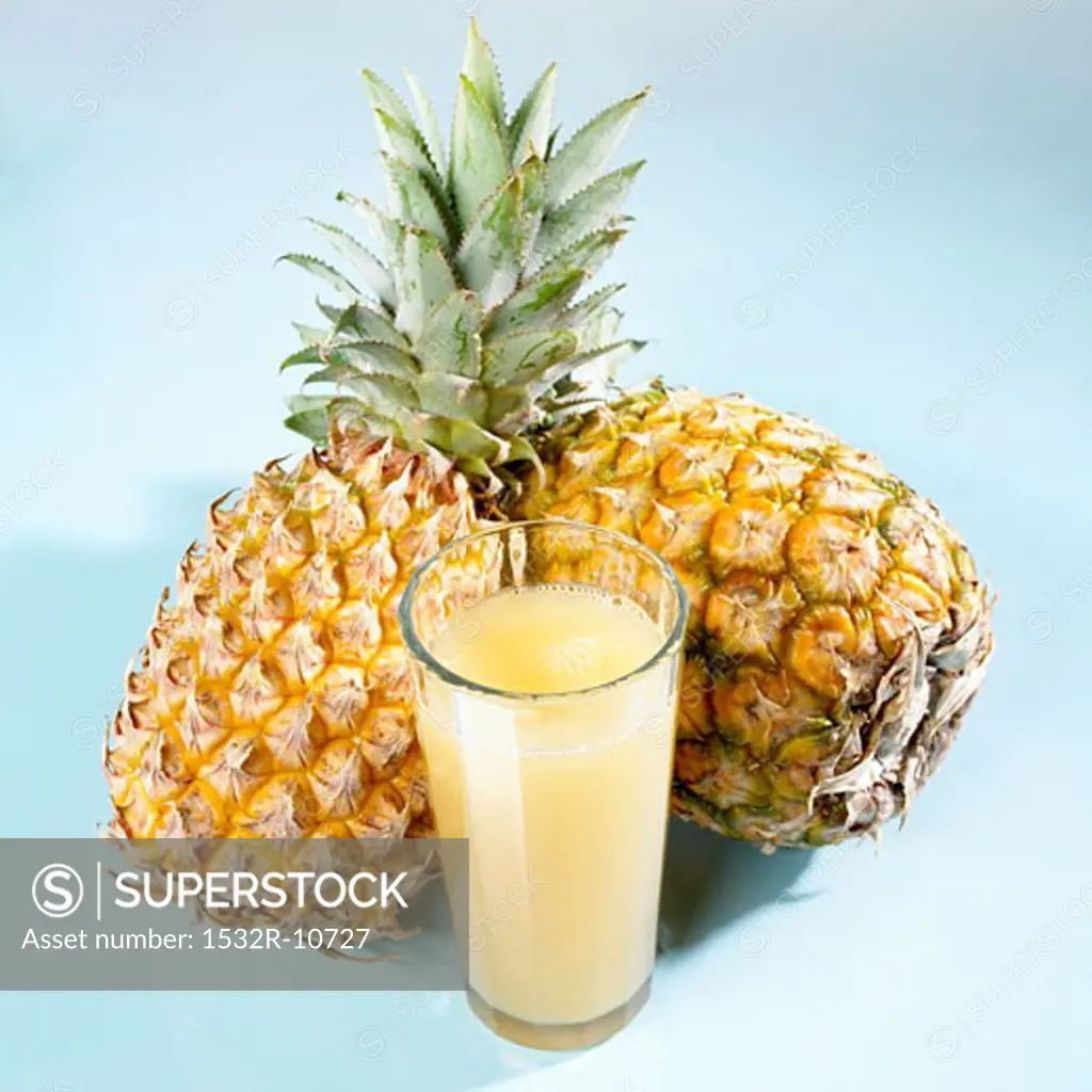 A glass of pineapple juice in front of two whole pineapples