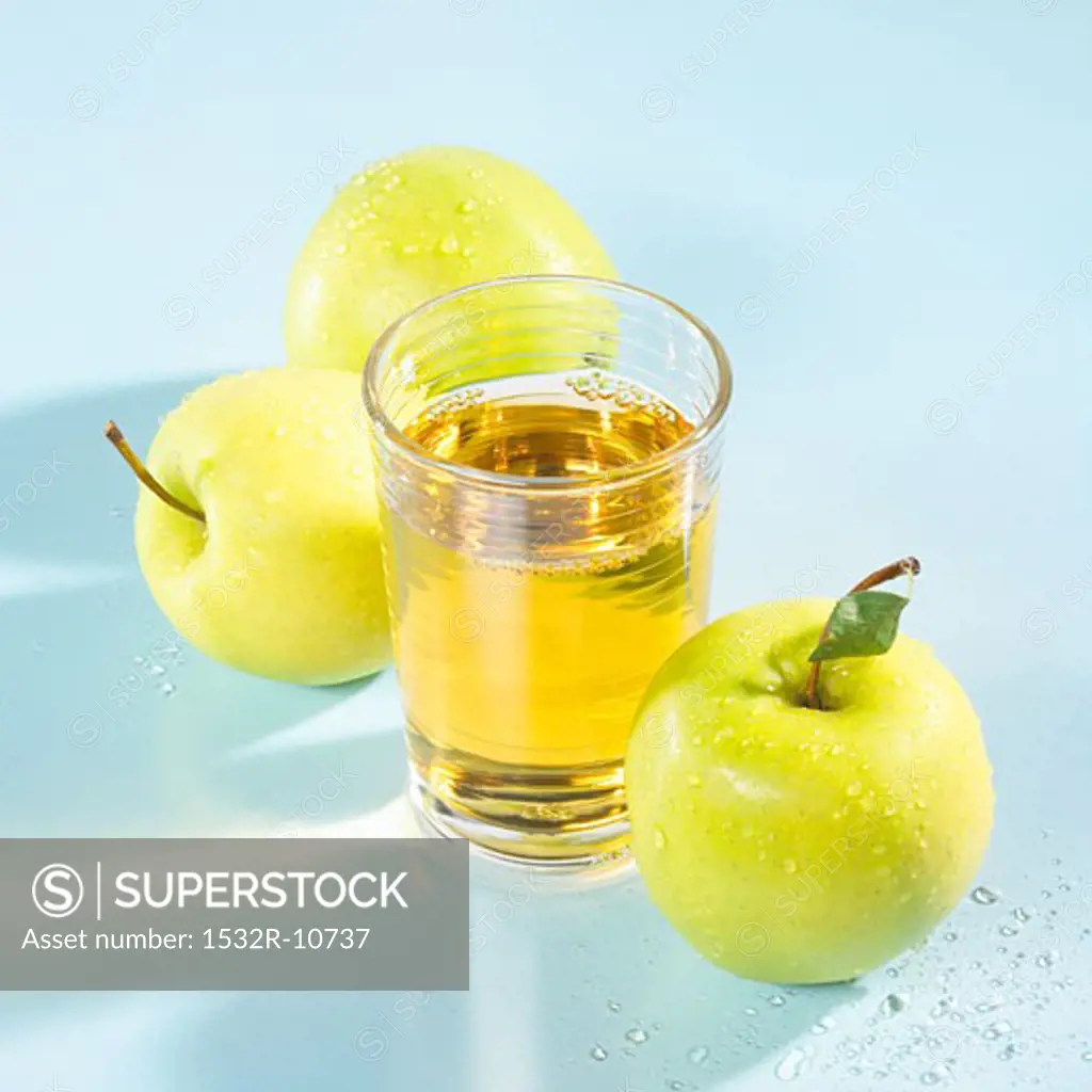 A glass of apple juice with apples beside it