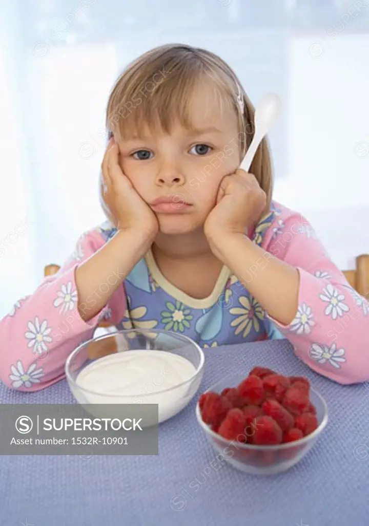 Girl sitting petulantly in front of yoghurt & raspberries