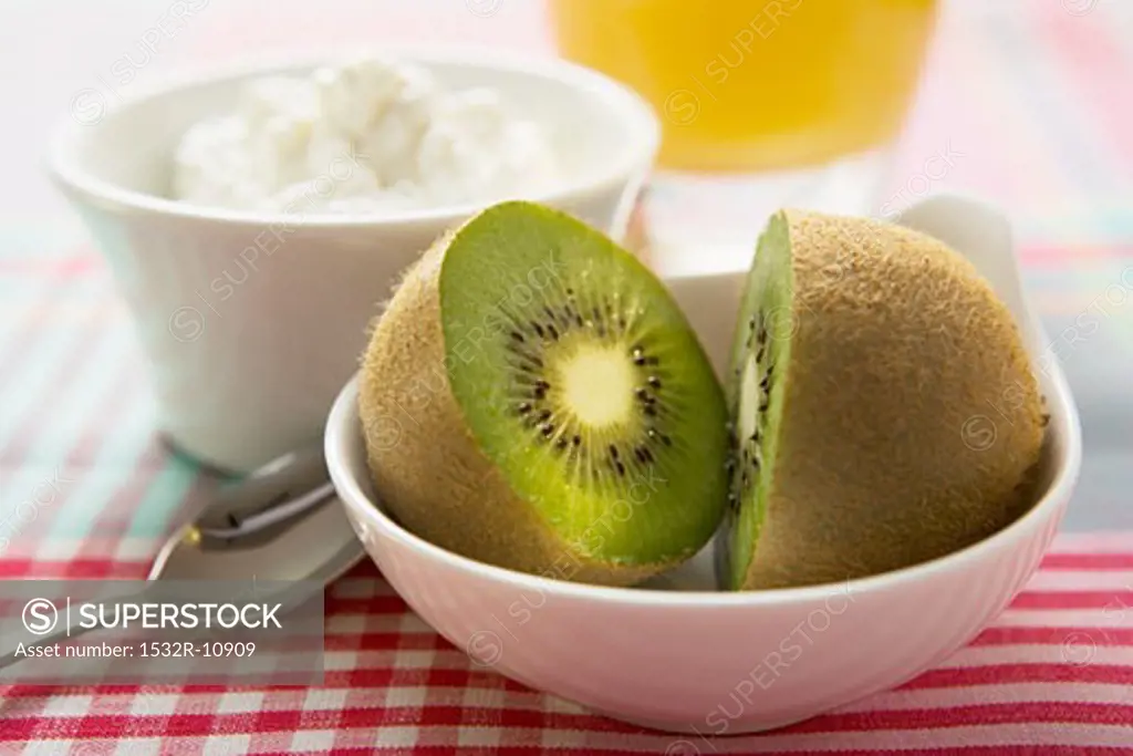 Halved kiwi fruit in front of a small bowl of cottage cheese