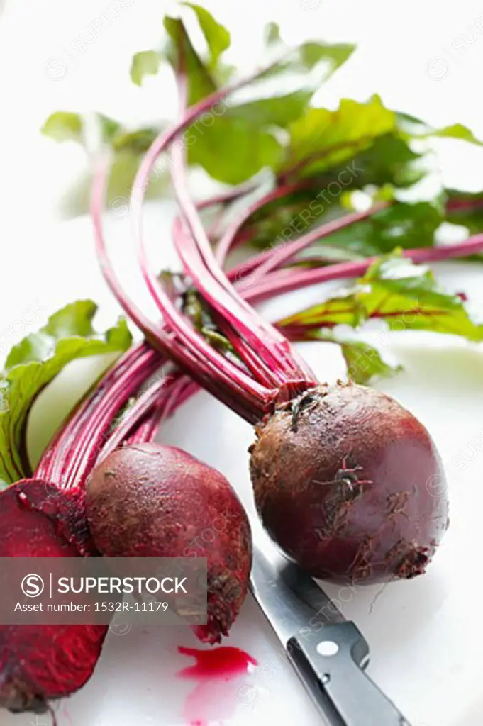 Beetroot with leaves, whole and halved; knife