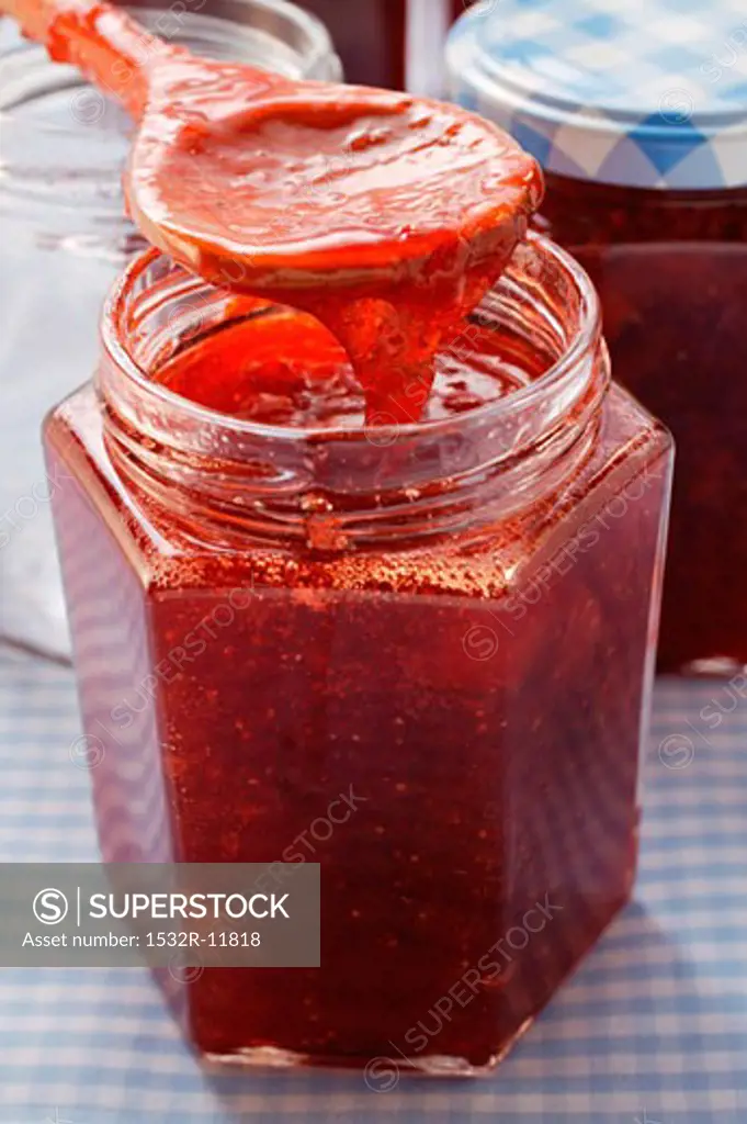 Strawberry jam in jar and on kitchen spoon