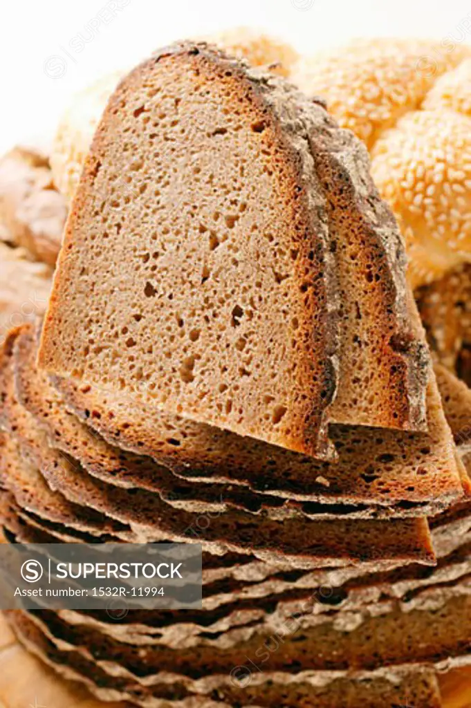 Slices of farmhouse bread in a pile in front of assorted rolls