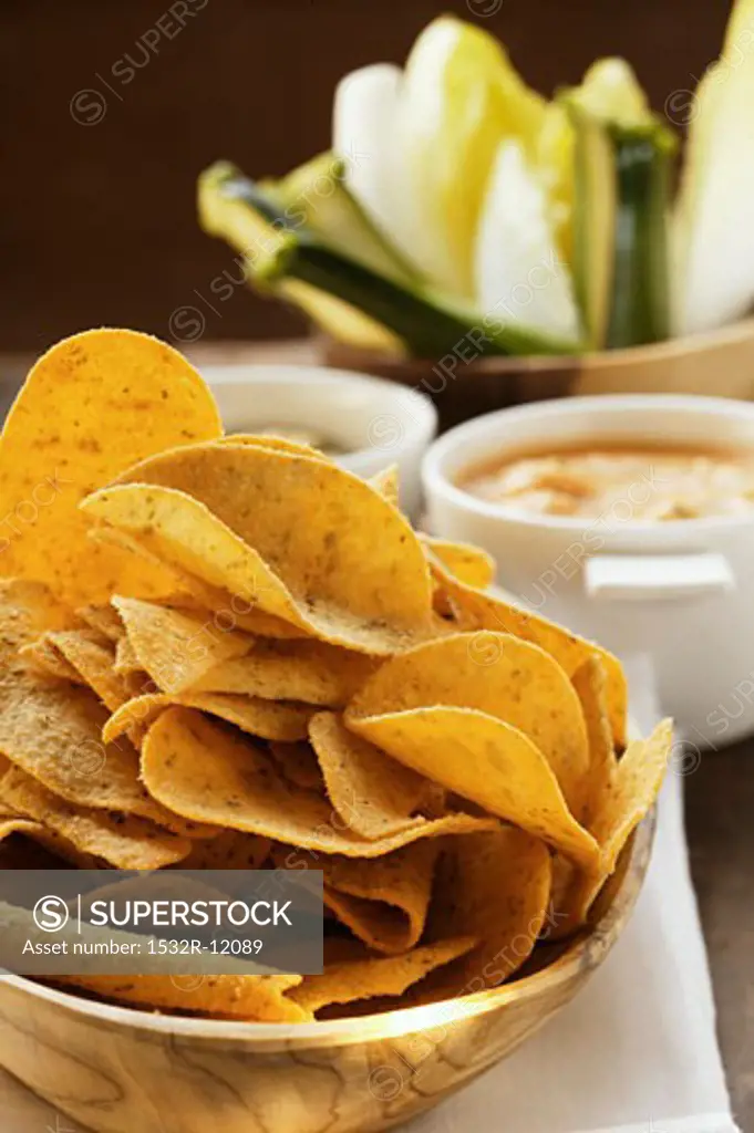 Tortilla chips in wooden bowl; dips; raw vegetables