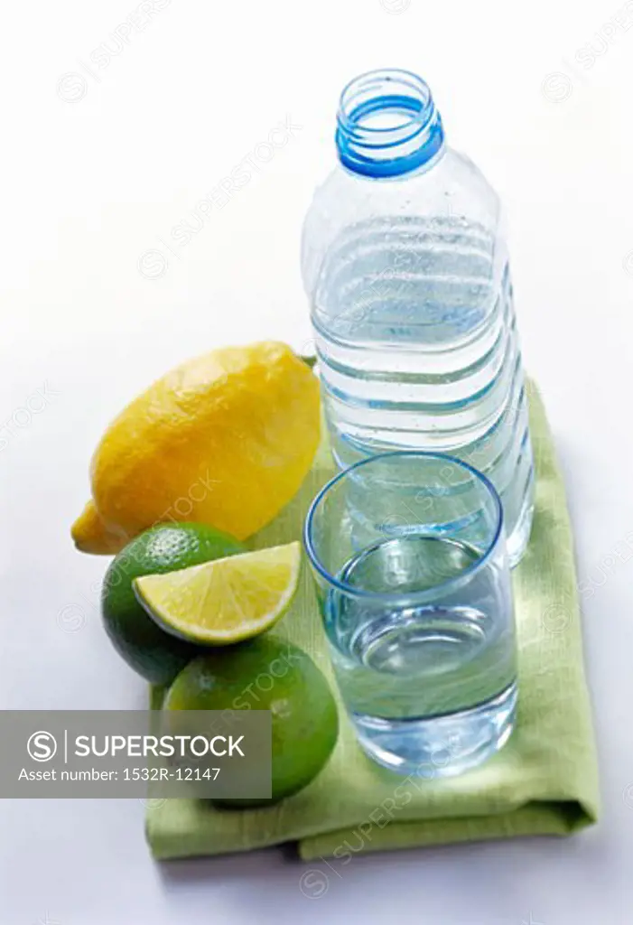Still water in bottle and glass beside lemon and limes