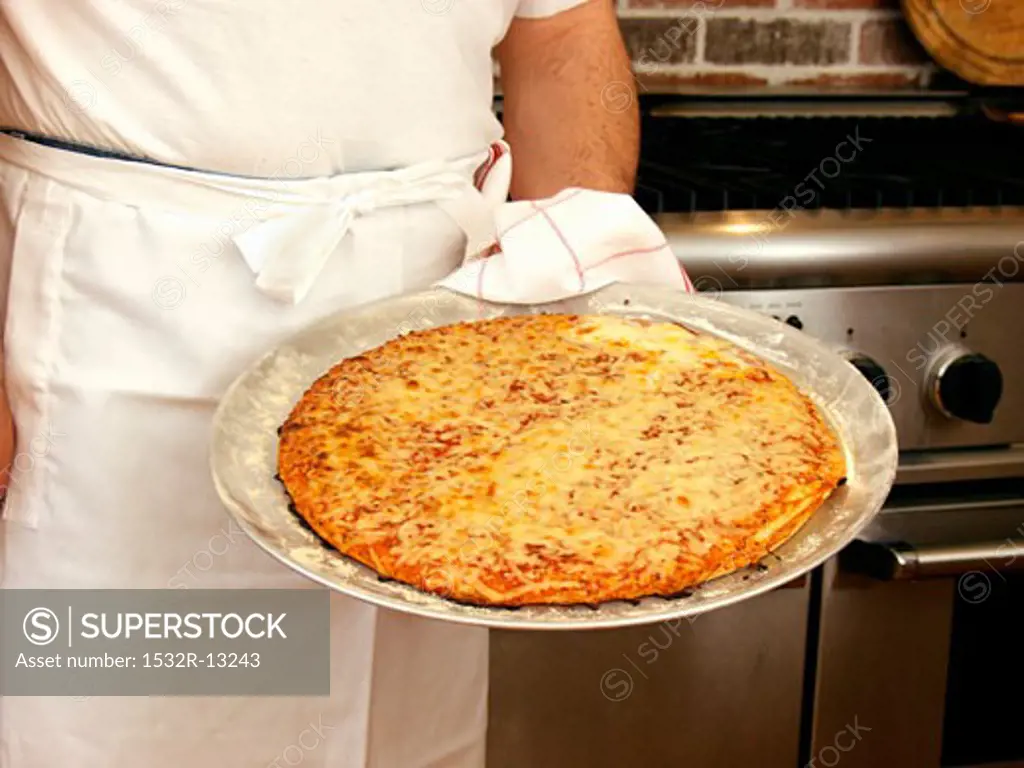 A Man Holding a Cheese Pizza in Front of Range