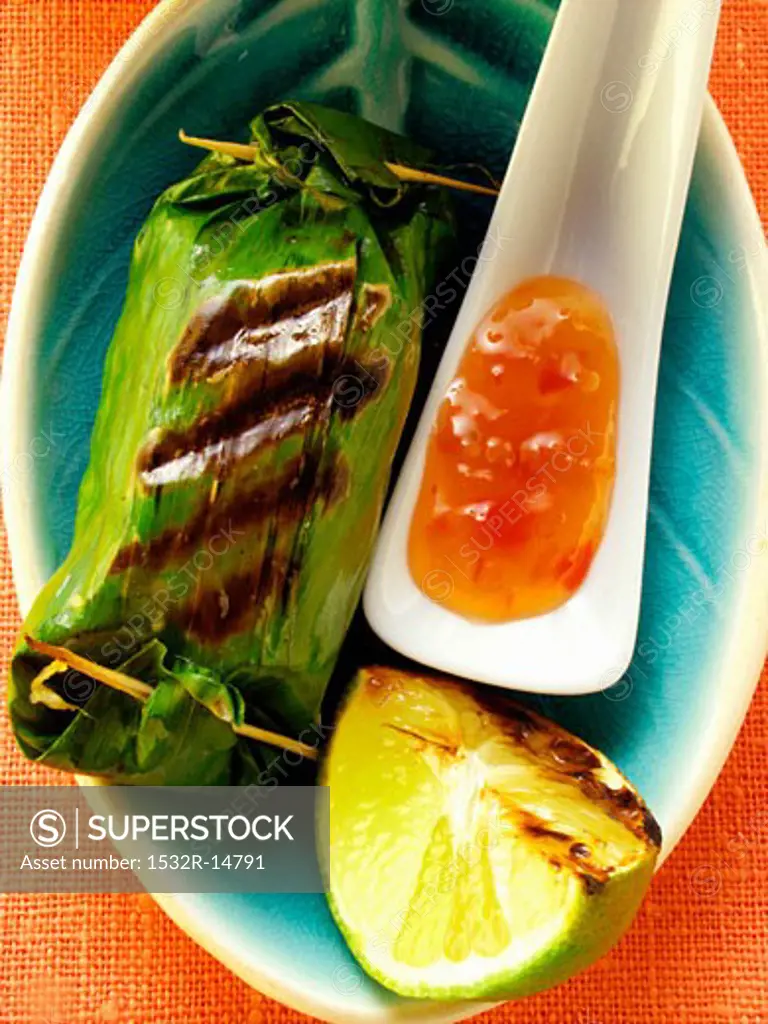 Rice parcels in banana leaf, chili sauce, lime