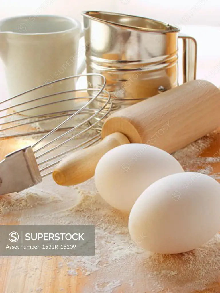 Various baking utensils, eggs and flour on chopping board