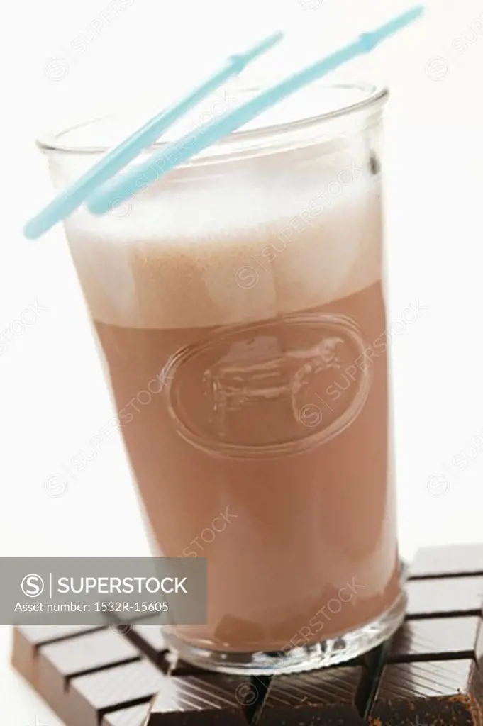Cocoa with milky froth in glass on bars of chocolate