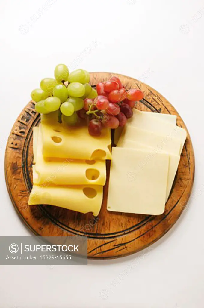 Emmental and American cheese with grapes on wooden plate