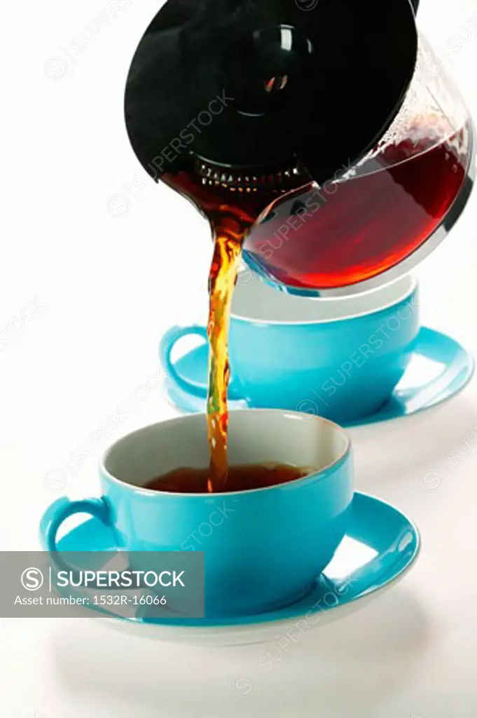 Pouring coffee out of glass coffee pot into blue cup
