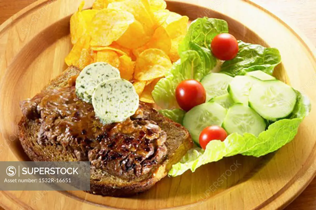 Steak with herb butter on bread, potato crisps and salad