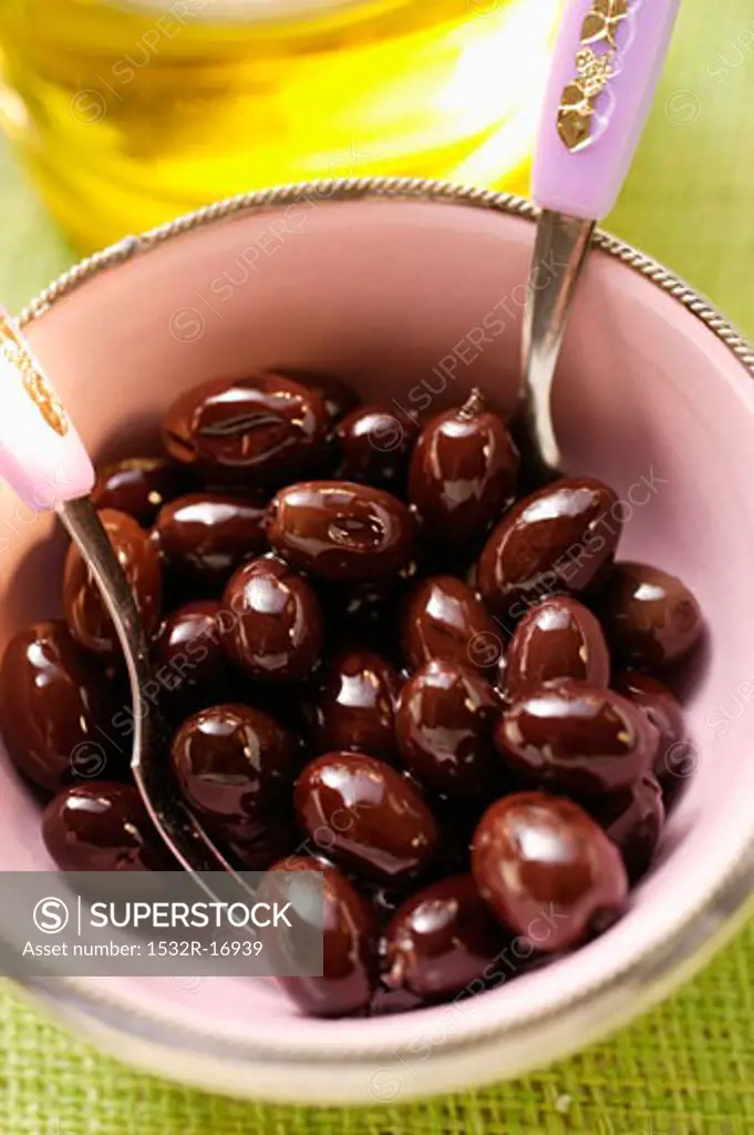 Pickled black olives in small bowl, olive oil behind