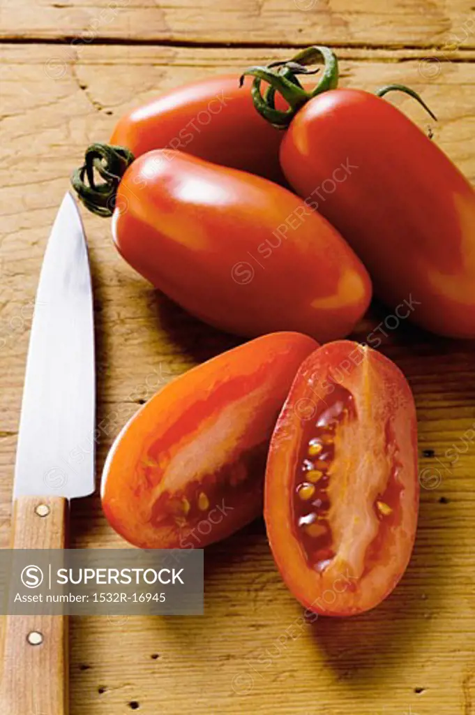 Four 'date' tomatoes on wooden background, one halved