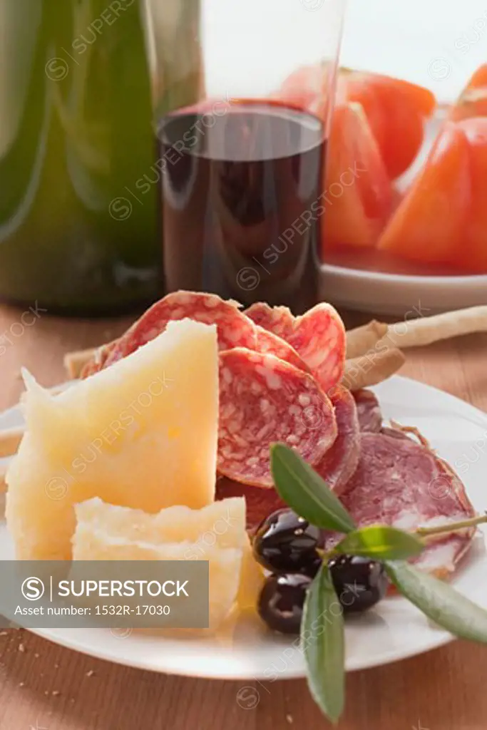 Salami, cheese, olives & grissini on plate, tomatoes, wine
