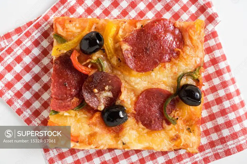 A slice of salami pizza with peppers and olives