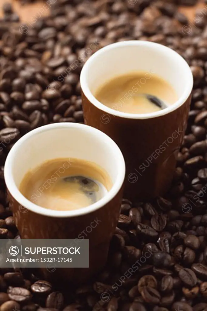 Two espressos standing on coffee beans
