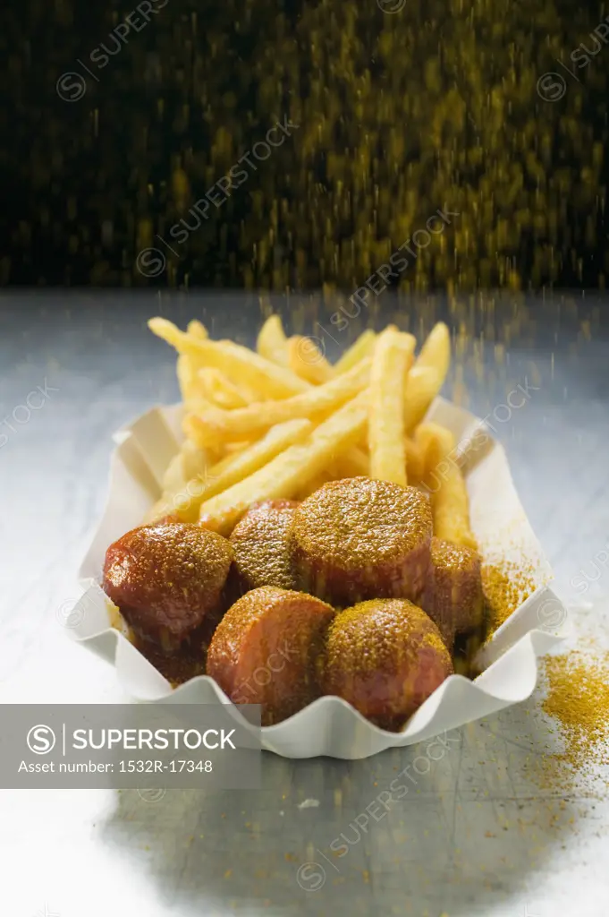 Sprinkling curry powder onto currywurst and chips