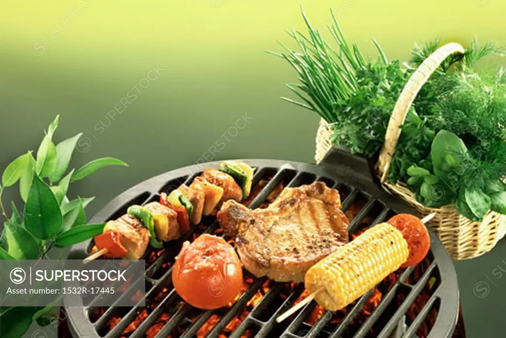 Chop, kebab, sweetcorn and tomato on barbecue; fresh herbs