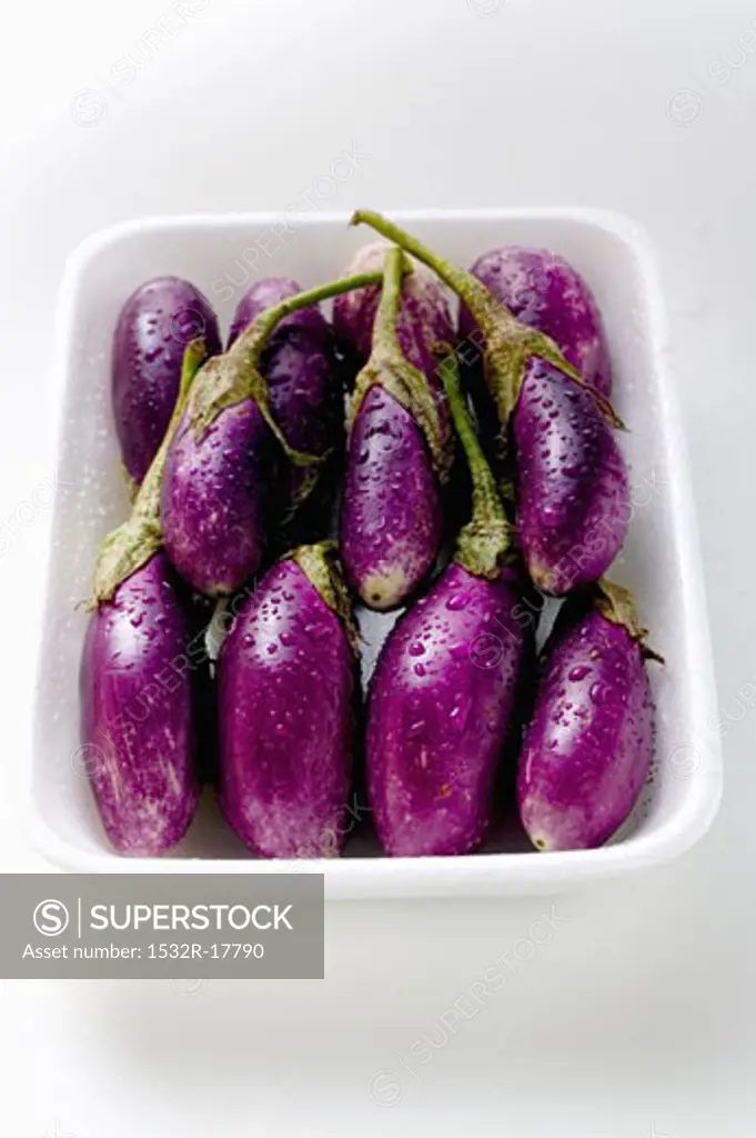 Baby aubergines with drops of water in white dish