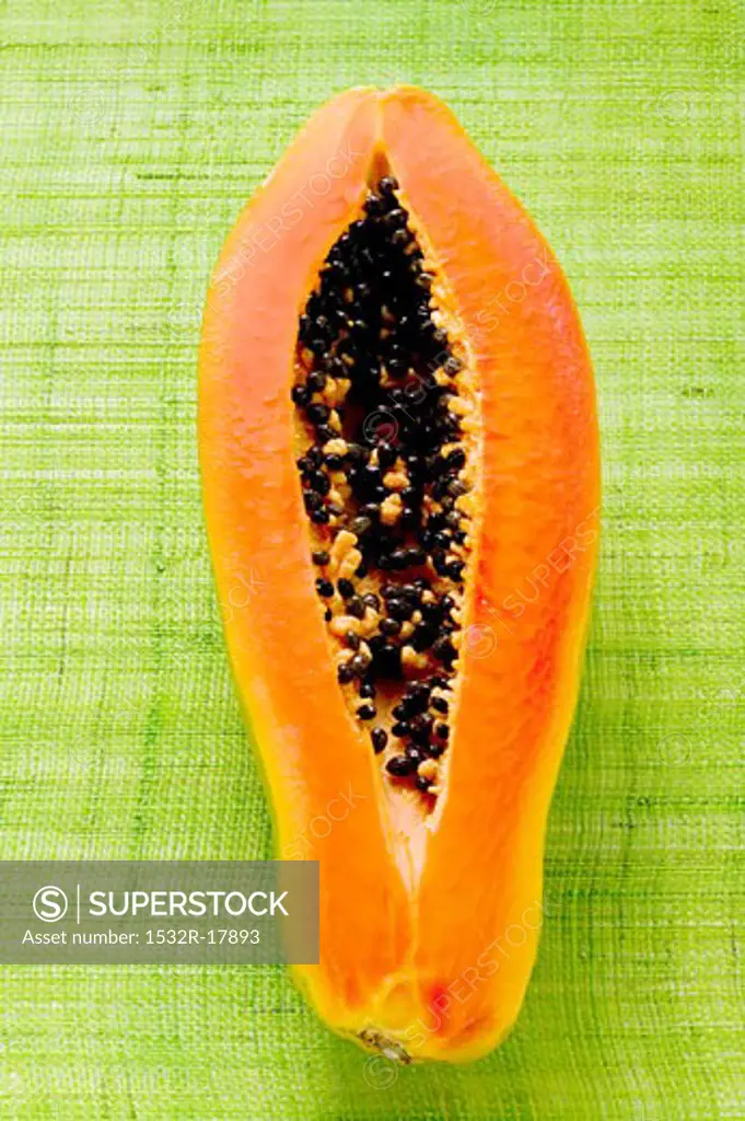 Half a papaya on green background