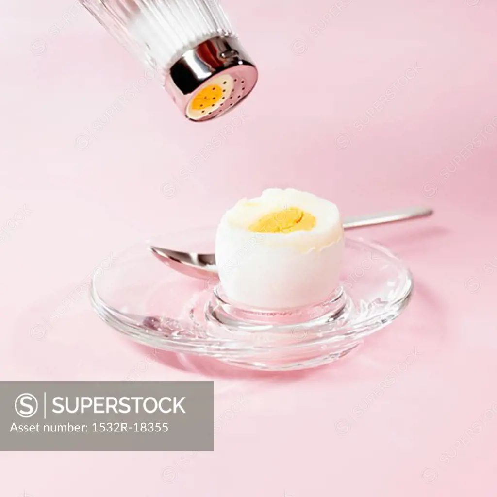 Breakfast egg with top knocked off, being sprinkled with salt