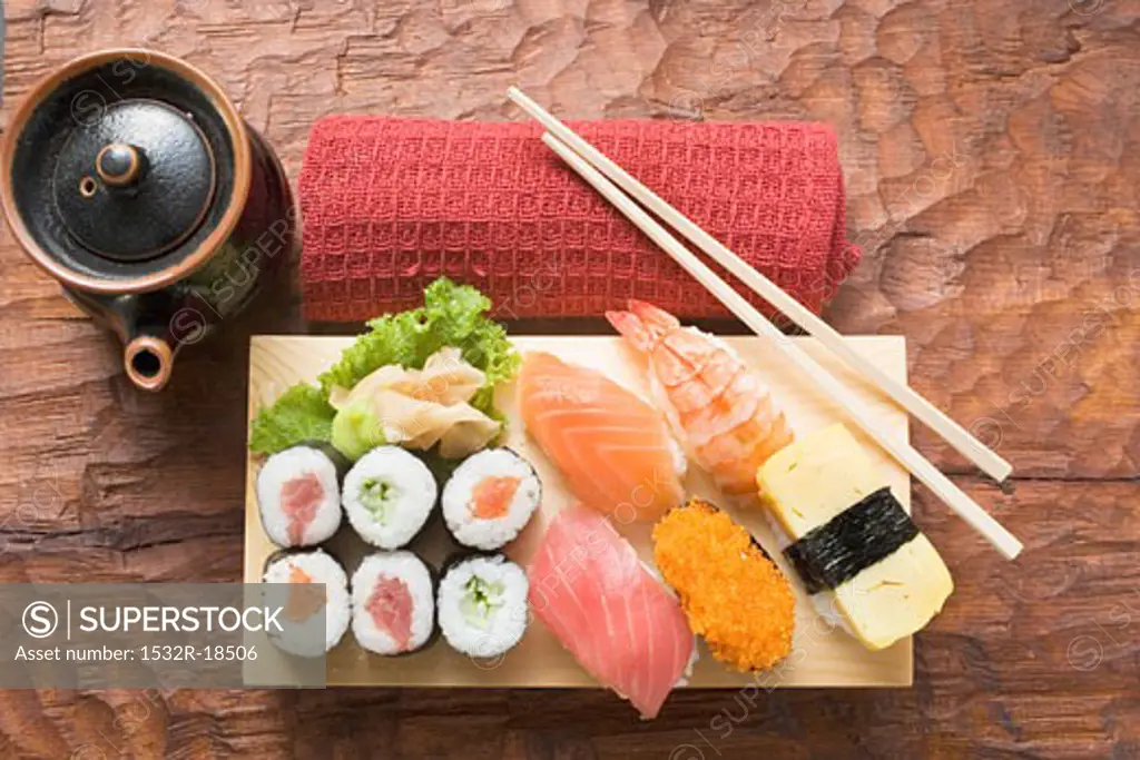 Assorted sushi on sushi board, hand towel and pot beside it