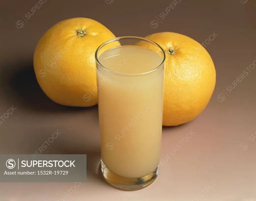 A glass of grapefruit juice and two grapefruits