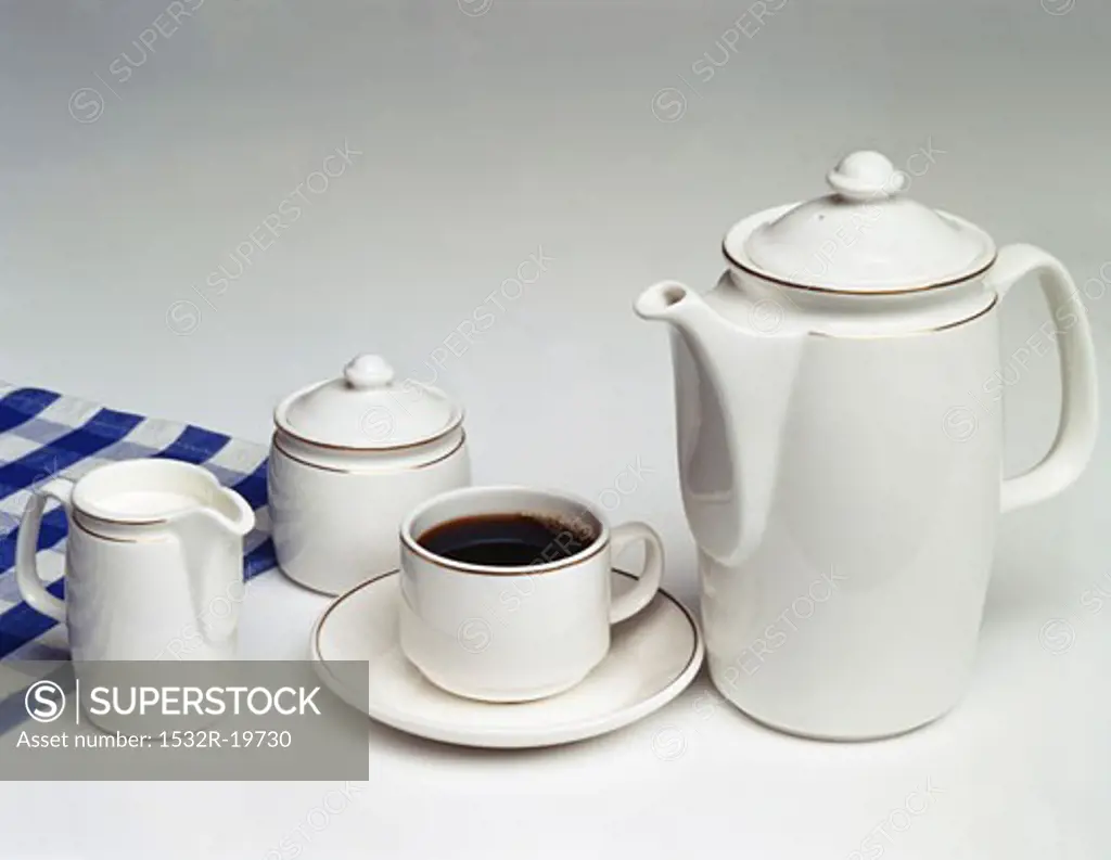A cup of coffee, coffee pot, sugar bowl and cream jug