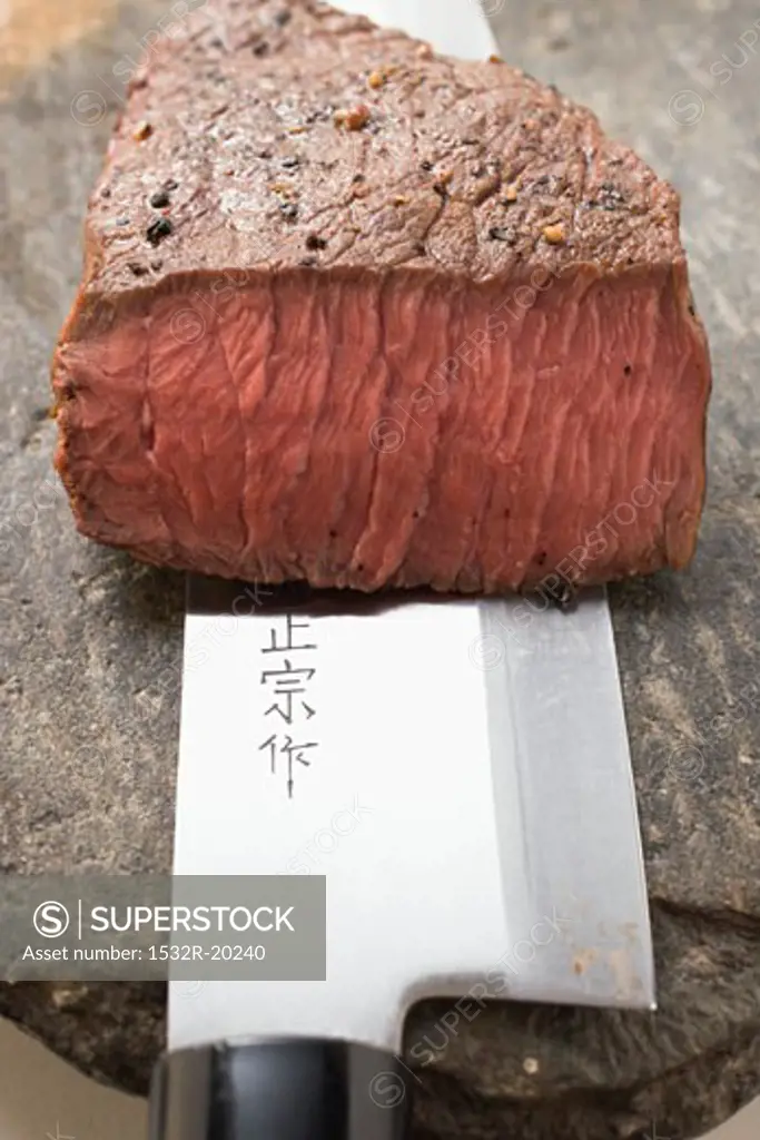 Beef steak with a piece cut off, on Asian knife