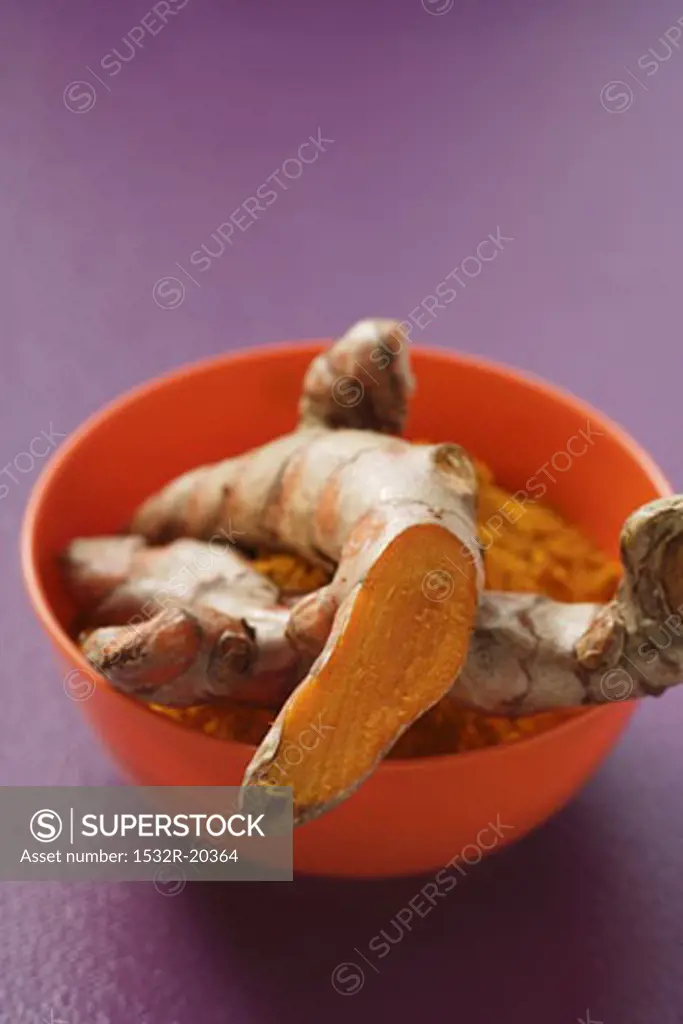 Turmeric roots and ground turmeric in orange bowl