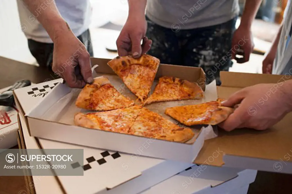 Workers taking pieces of pizza out of pizza box