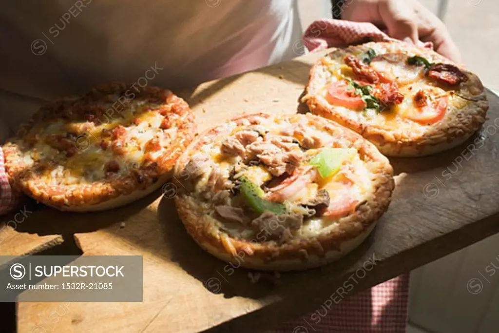 Person holding wooden board with three different mini-pizzas