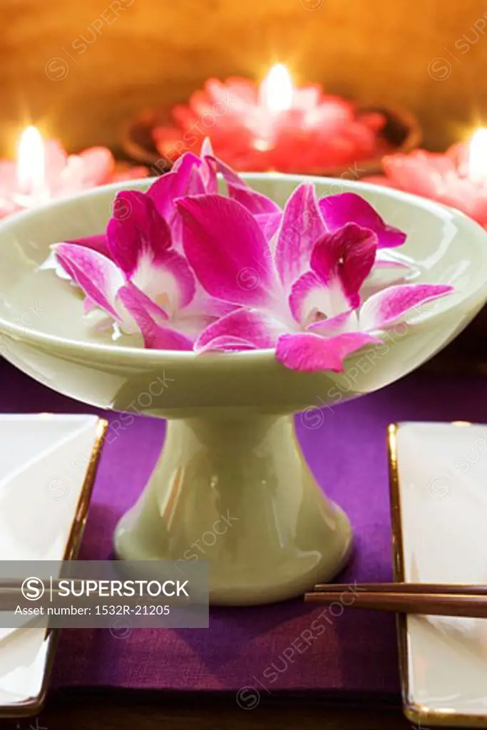 Thai table decoration: orchids in bowl of water, candles