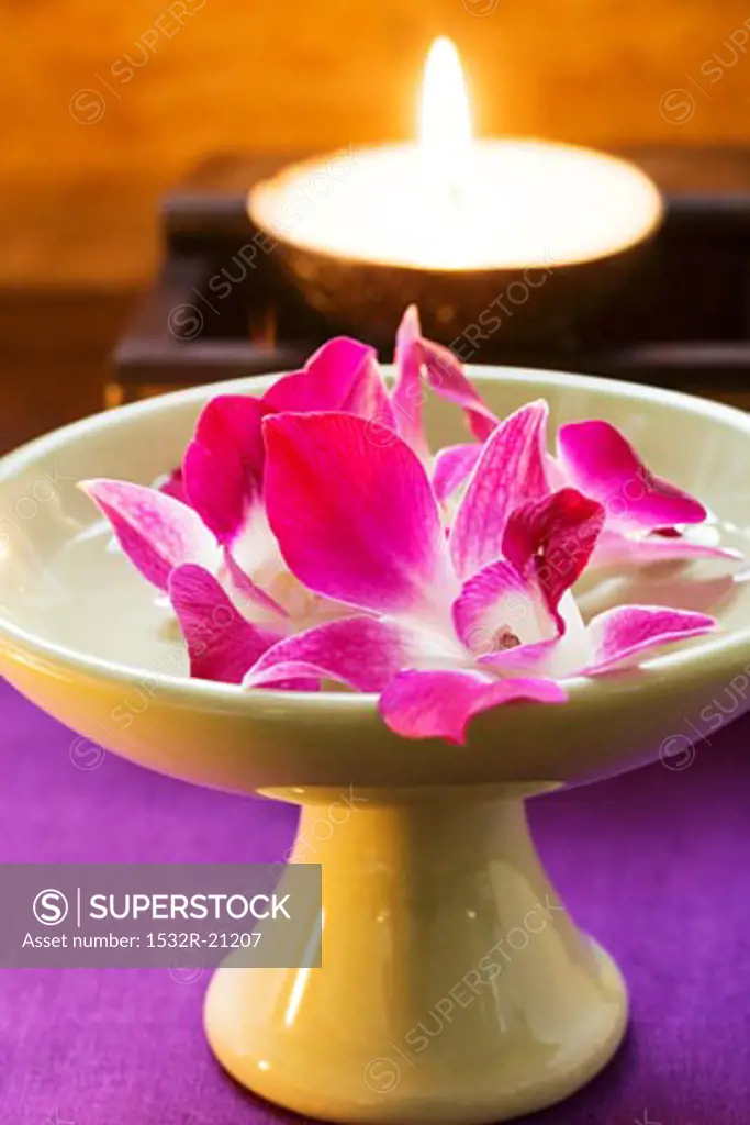Thai table decoration: orchids in bowl of water, candle