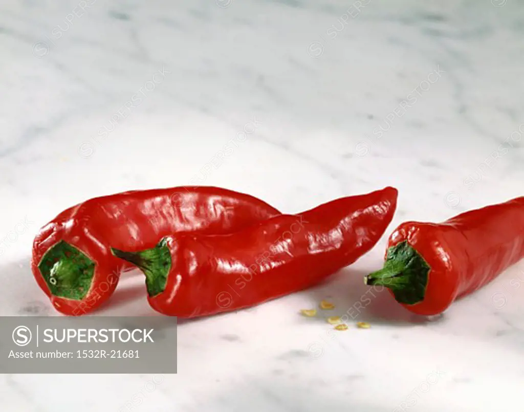 Three red chili peppers on a marble slab