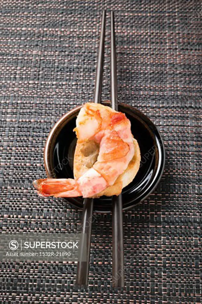 Bacon-wrapped king prawn on white bread and chopsticks