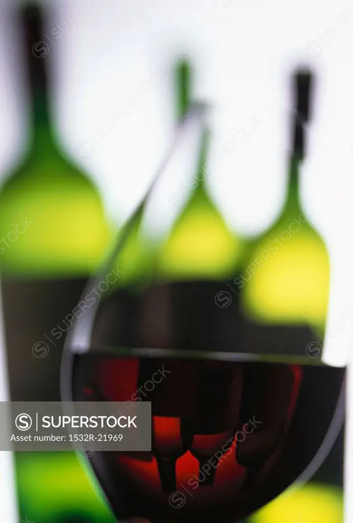 Glass of red wine in front of wine bottles