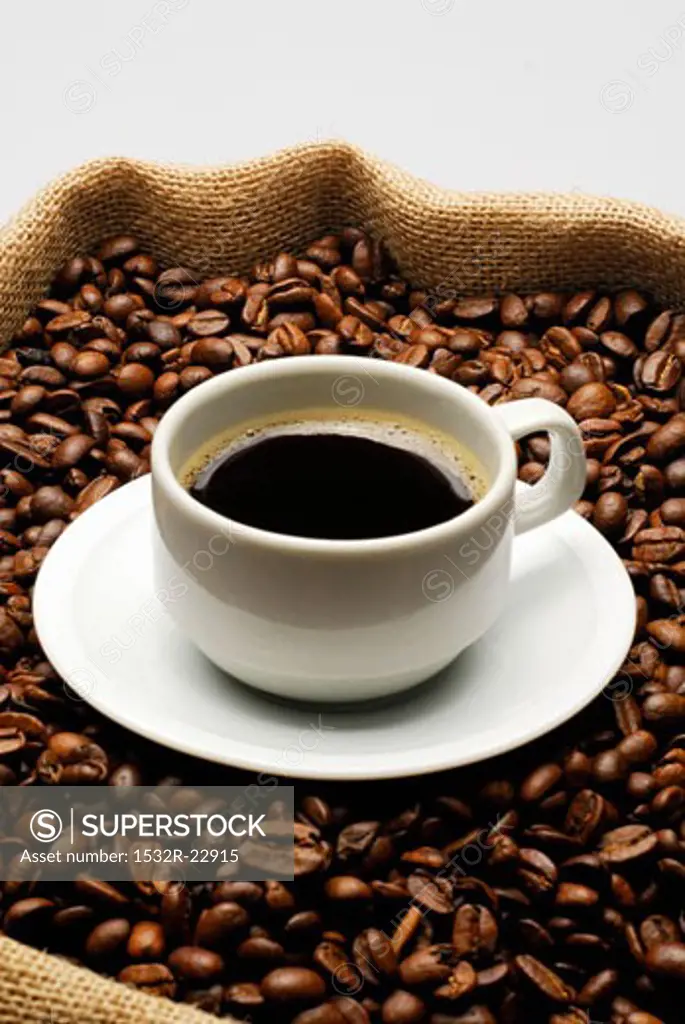 A cup of coffee on a jute sack full of coffee beans