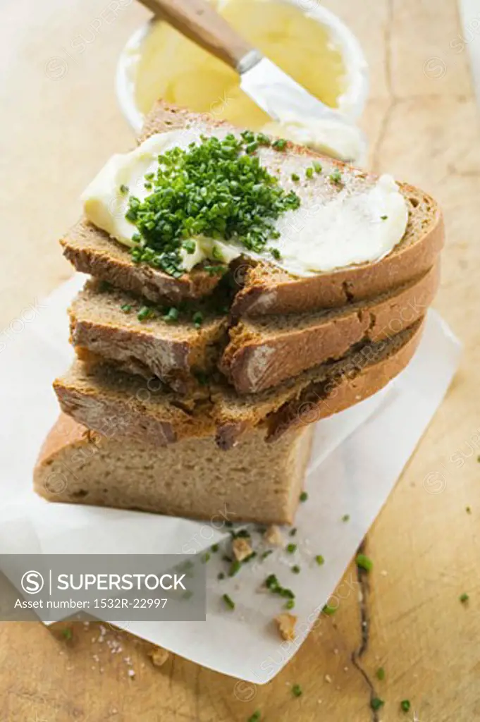 Several slices of bread in a pile with butter and chives