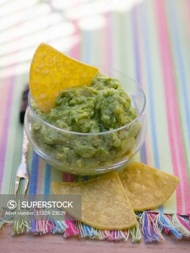 Guacamole in a small glass bowl with nachos