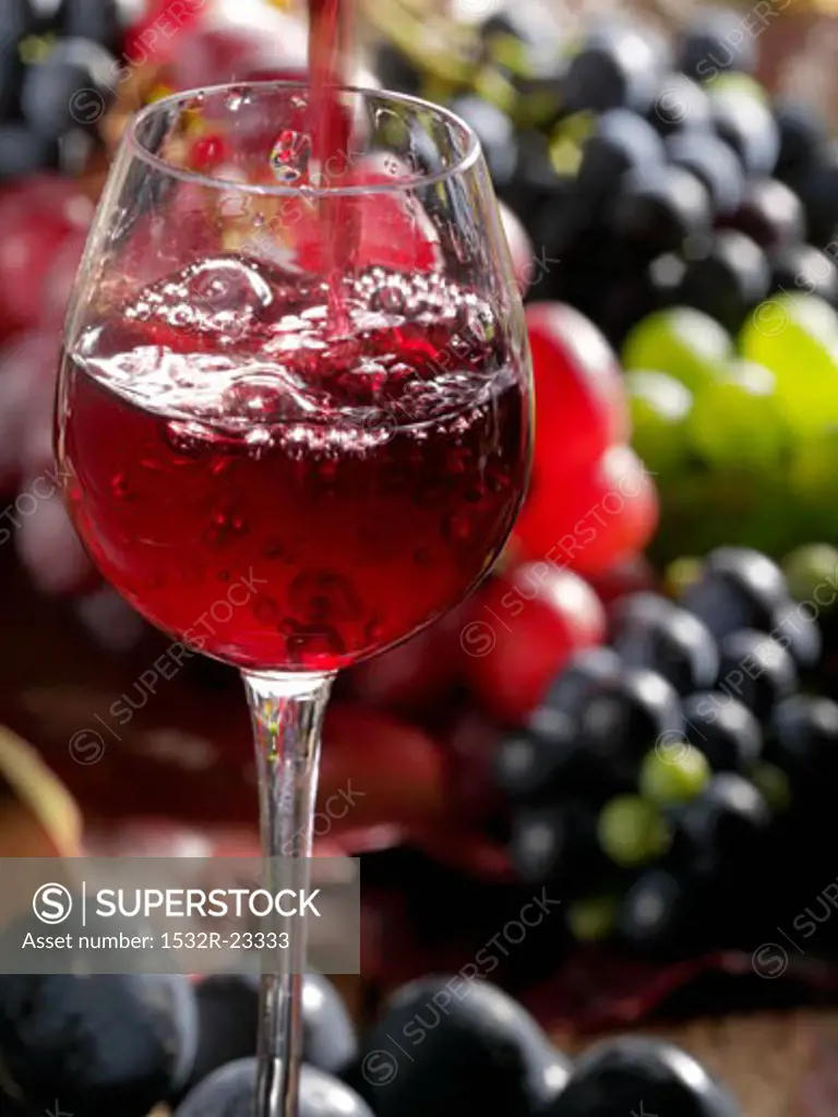 Pouring a glass of red wine with grapes in the background