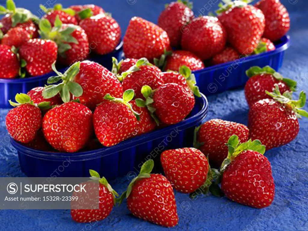 Three punnets of strawberries with strawberries beside them