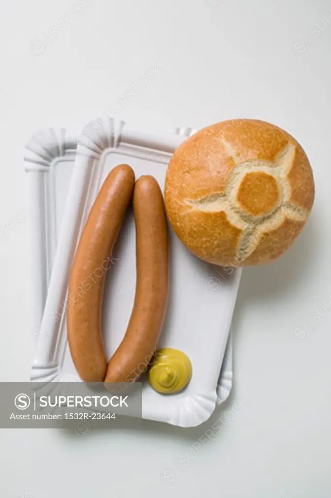 Sausages with mustard and roll on two paper plates