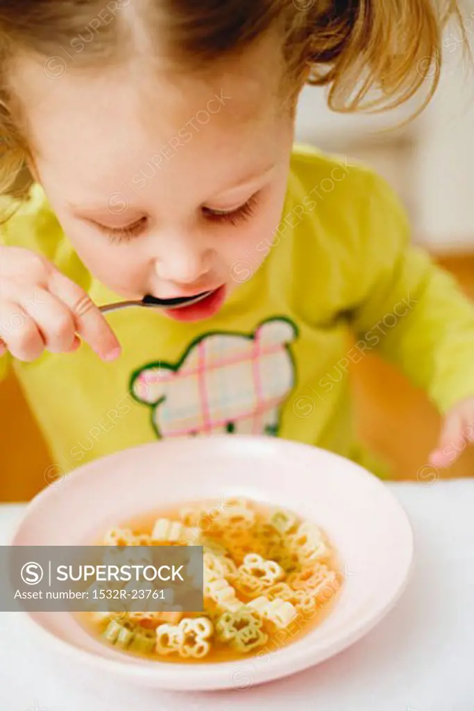 Small girl eating teddy bear noodle soup