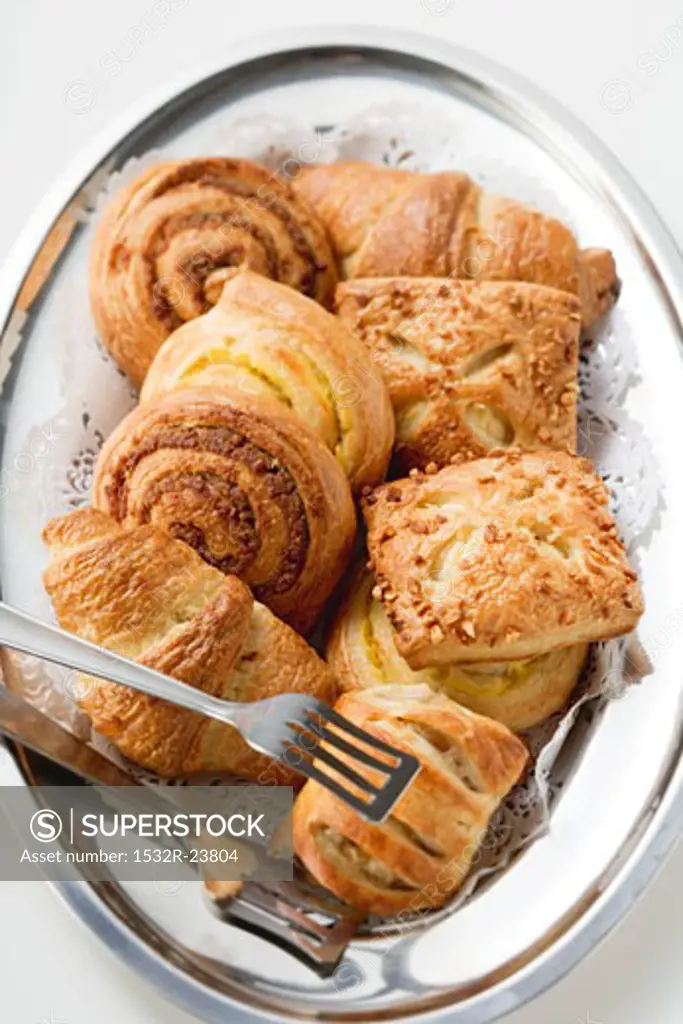 Assorted Danish pastries on silver platter with cake tongs