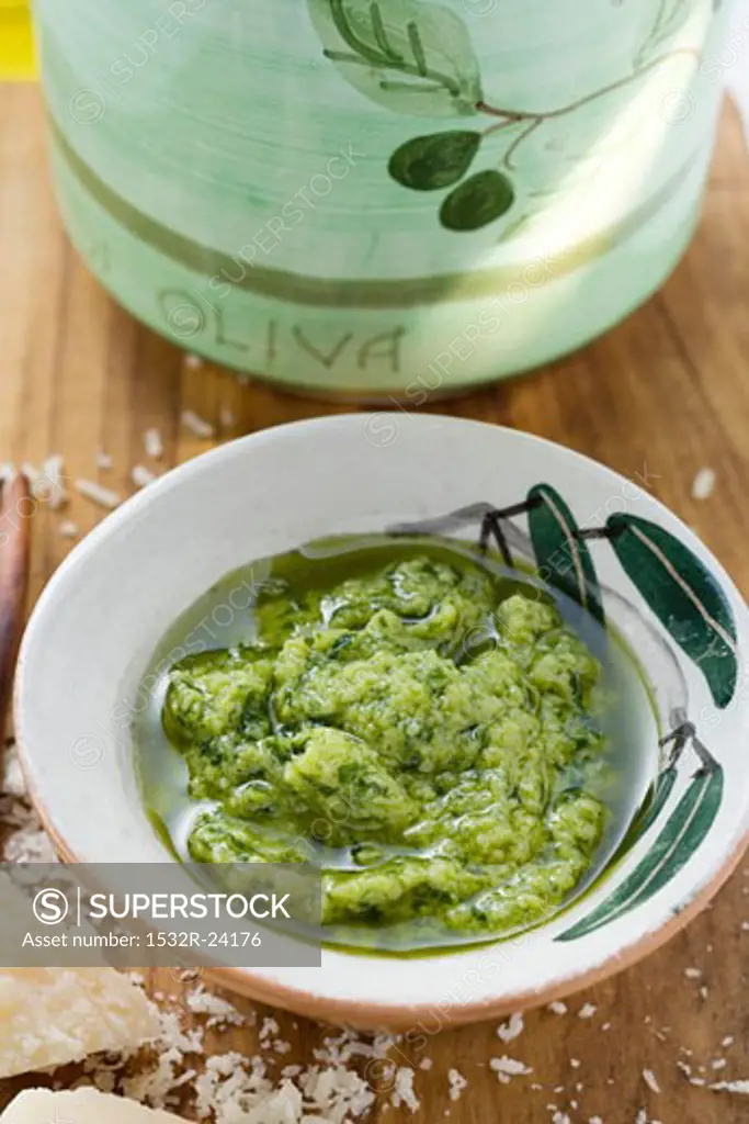 Pesto with olive oil in small bowl, Parmesan