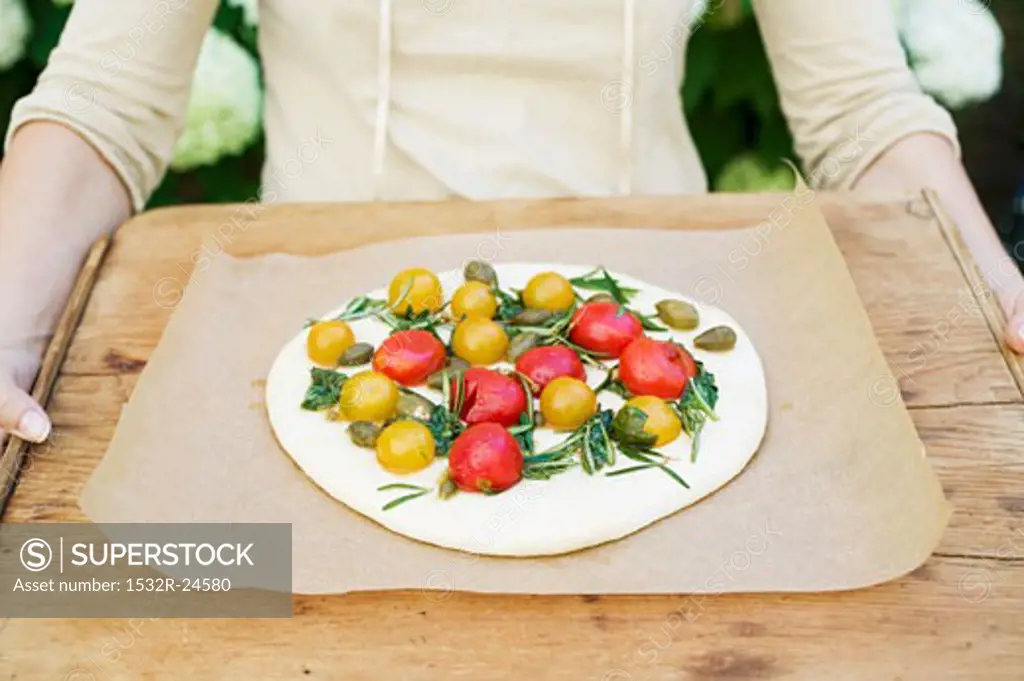 Person holding wooden board with unbaked pizza