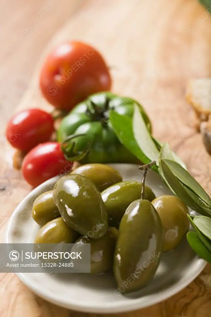 Green olives on plate, a few tomatoes behind