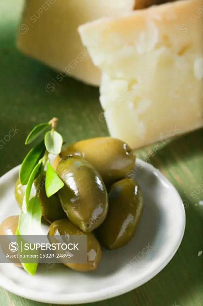 Green olives with olive sprig on plate, cheese in background